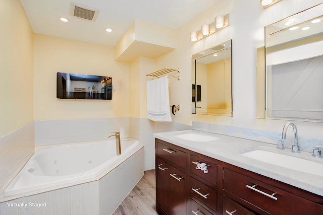 bathroom featuring a whirlpool tub, wood finished floors, visible vents, double vanity, and a sink