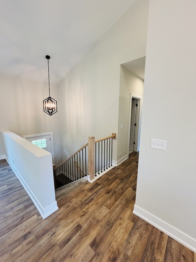 hallway featuring an upstairs landing, a chandelier, wood finished floors, baseboards, and a towering ceiling