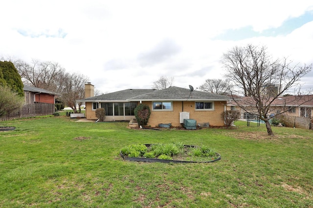rear view of house with a sunroom, a yard, fence, and brick siding
