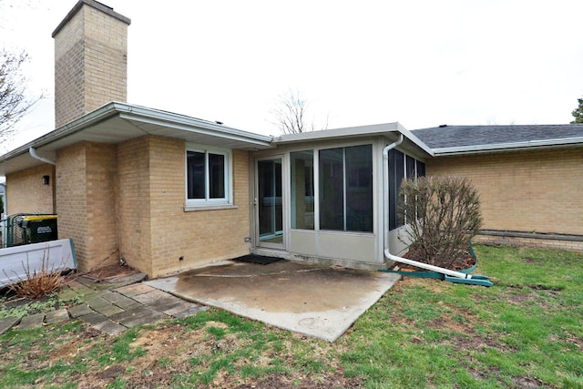 rear view of property featuring a sunroom, a patio area, a lawn, a chimney, and brick siding