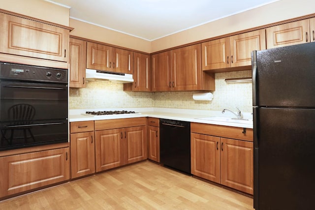 kitchen featuring under cabinet range hood, light wood finished floors, a sink, and black appliances