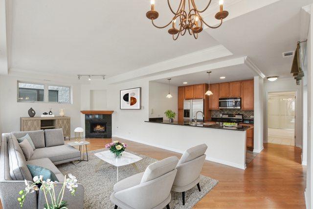 2317 W Wolfram St Unit 211, Chicago, IL 60618 - living room with light wood-style flooring, a lit fireplace, rail lighting, crown molding, and a chandelier