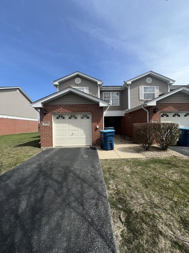 view of front of home featuring an attached garage, driveway, a front yard, and brick siding