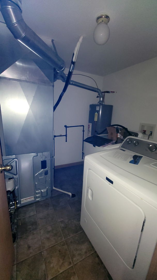 laundry area featuring washer / clothes dryer, laundry area, dark tile patterned floors, and water heater