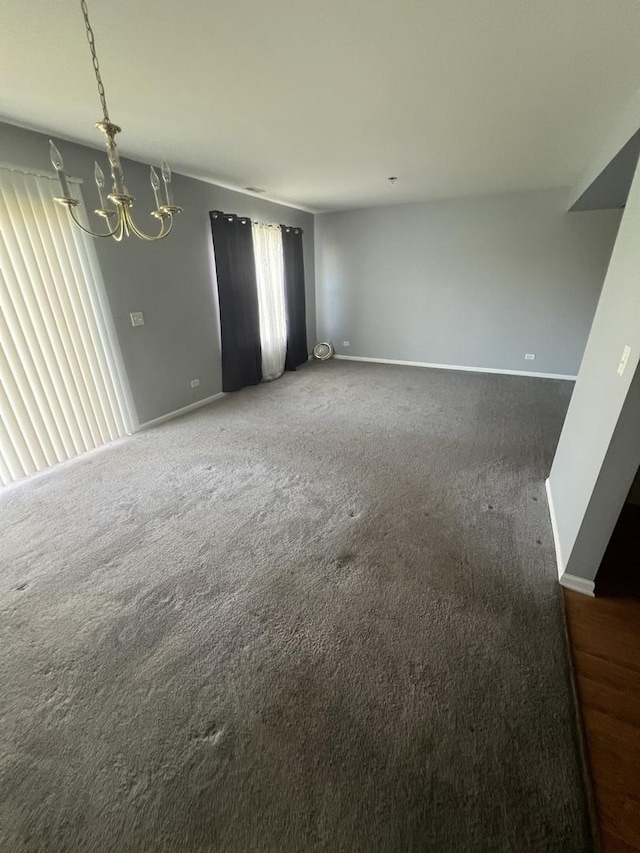 carpeted empty room featuring a notable chandelier and baseboards