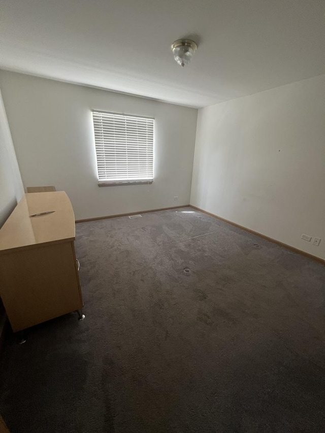 spare room featuring dark carpet and baseboards