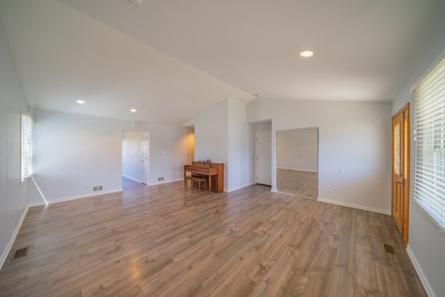 empty room with lofted ceiling, visible vents, baseboards, and wood finished floors