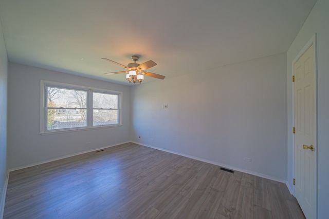 empty room featuring wood finished floors, visible vents, a ceiling fan, and baseboards