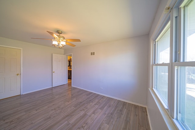 empty room with visible vents, wood finished floors, ceiling fan, and a healthy amount of sunlight