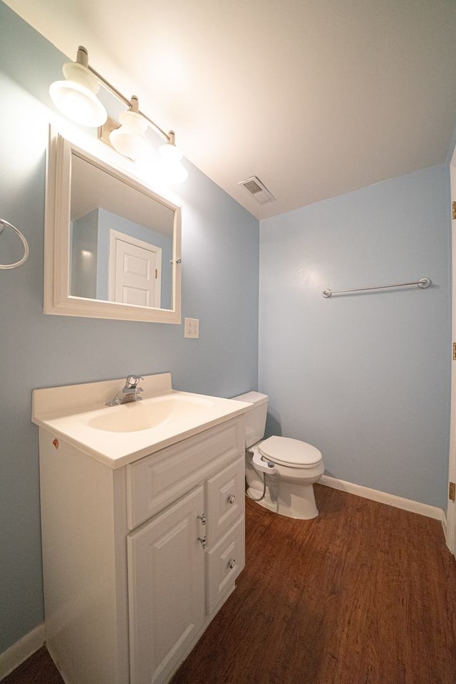 bathroom with wood finished floors, vanity, baseboards, toilet, and visible vents