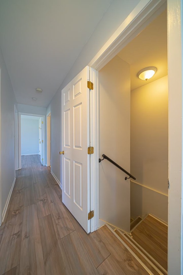 hall featuring an upstairs landing, baseboards, and wood finished floors