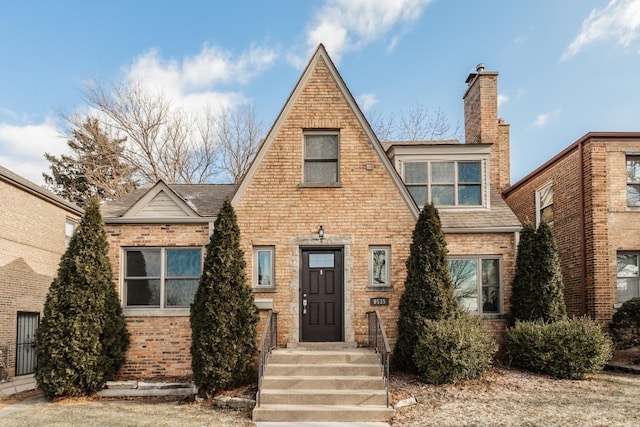tudor-style house featuring roof with shingles, a chimney, and brick siding