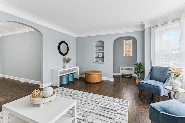 living area with arched walkways, built in features, radiator heating unit, and wood finished floors