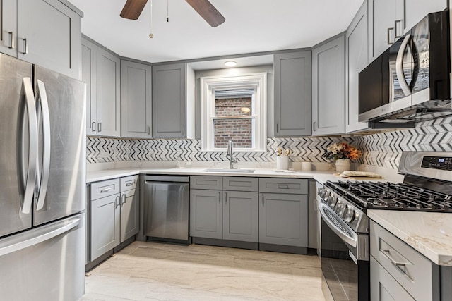 kitchen featuring tasteful backsplash, appliances with stainless steel finishes, gray cabinetry, ceiling fan, and a sink