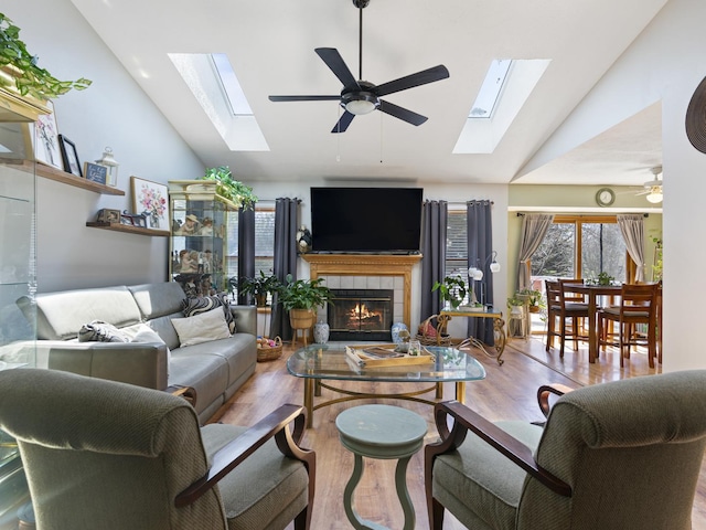 living area with lofted ceiling with skylight, a ceiling fan, a tiled fireplace, and wood finished floors
