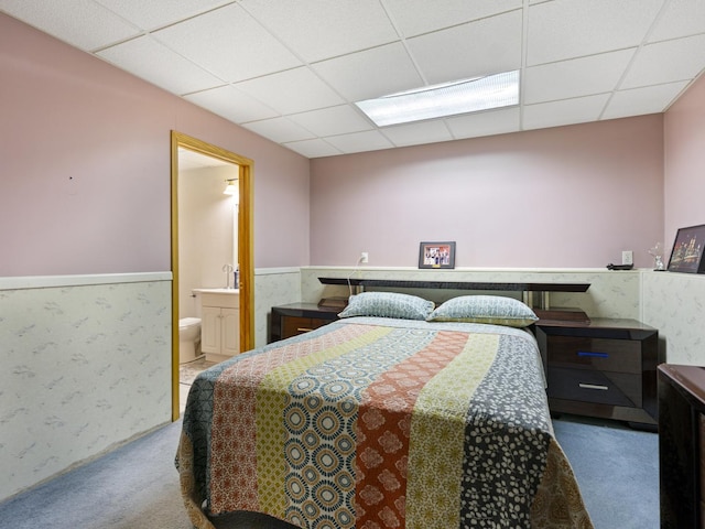 bedroom with a drop ceiling, ensuite bathroom, a wainscoted wall, and carpet floors
