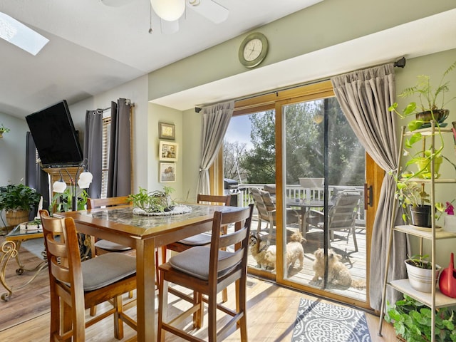 dining room with ceiling fan, vaulted ceiling with skylight, and light wood-style flooring