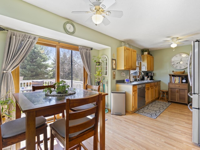 kitchen with light wood-style flooring, a sink, appliances with stainless steel finishes, ceiling fan, and dark countertops