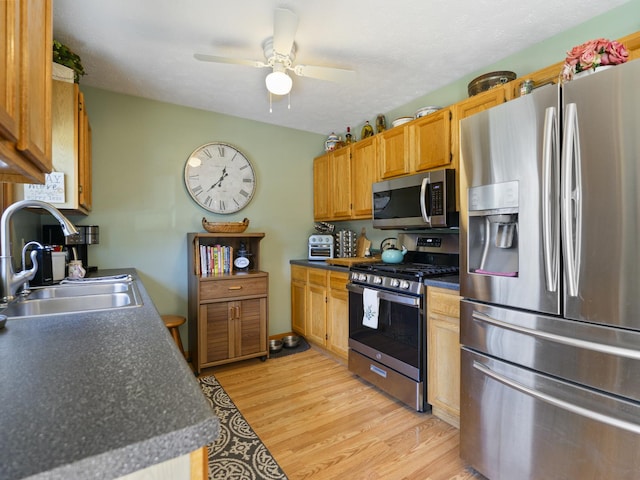 kitchen with a sink, dark countertops, ceiling fan, stainless steel appliances, and light wood-type flooring