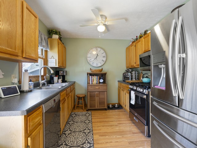 kitchen featuring a sink, ceiling fan, light wood-style flooring, dark countertops, and appliances with stainless steel finishes