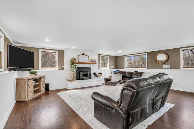 living room featuring dark wood-type flooring, a healthy amount of sunlight, a brick fireplace, and a wainscoted wall