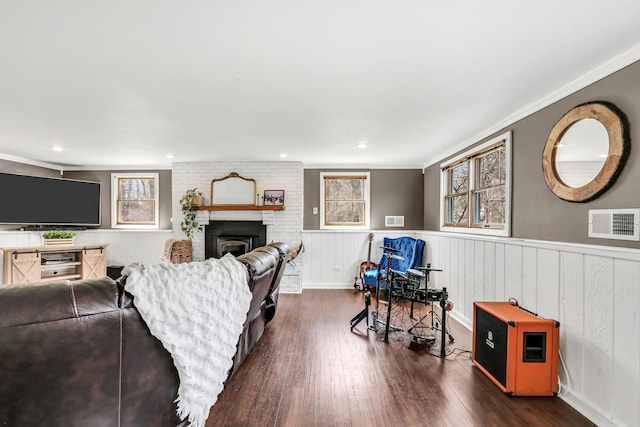 living area with visible vents, a brick fireplace, ornamental molding, dark wood-style floors, and a wainscoted wall