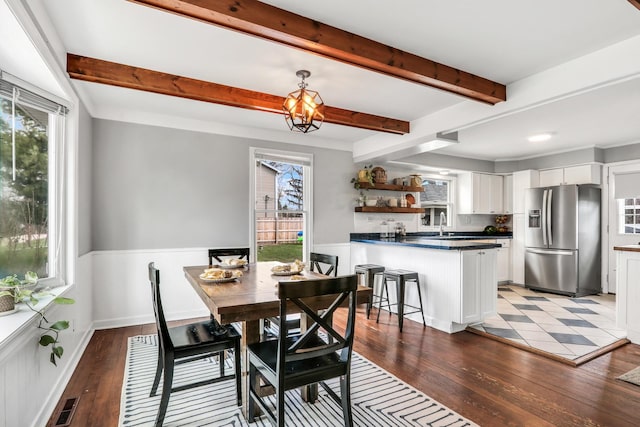 dining area featuring visible vents, beamed ceiling, a wainscoted wall, and wood finished floors