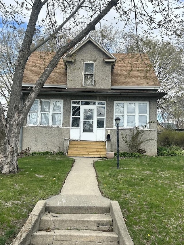 view of front facade featuring entry steps, roof with shingles, a front yard, and stucco siding