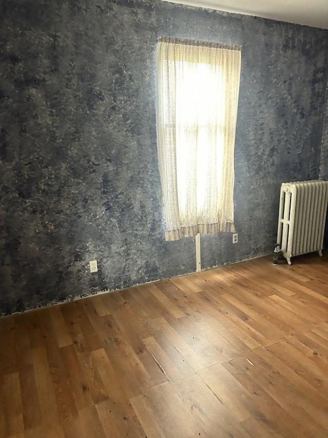 unfurnished room featuring radiator heating unit and hardwood / wood-style floors