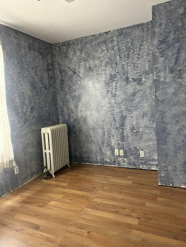 spare room with radiator heating unit and wood finished floors