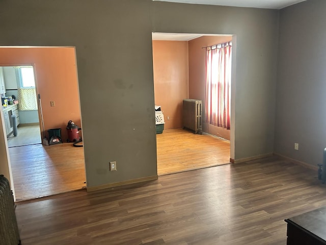 empty room with baseboards, wood finished floors, and radiator