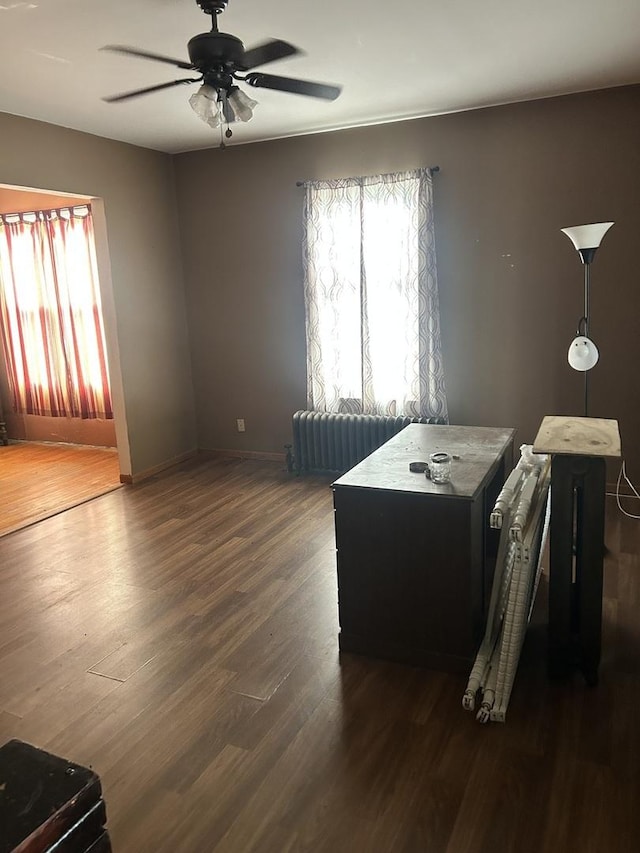 interior space featuring radiator heating unit, a ceiling fan, baseboards, and dark wood-type flooring