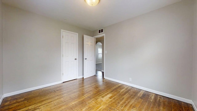 spare room featuring arched walkways, baseboards, visible vents, and wood finished floors