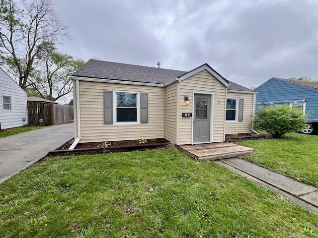 bungalow with a shingled roof, fence, and a front yard