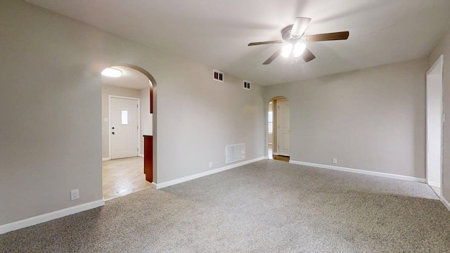 spare room with light carpet, arched walkways, a ceiling fan, baseboards, and visible vents
