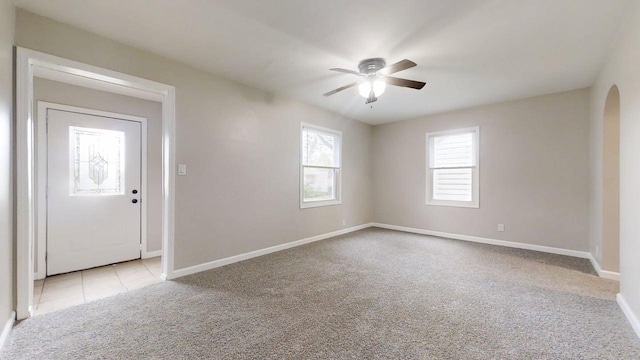 unfurnished room featuring baseboards, a ceiling fan, arched walkways, and light carpet