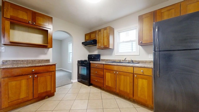 kitchen with brown cabinets, a sink, arched walkways, under cabinet range hood, and black appliances