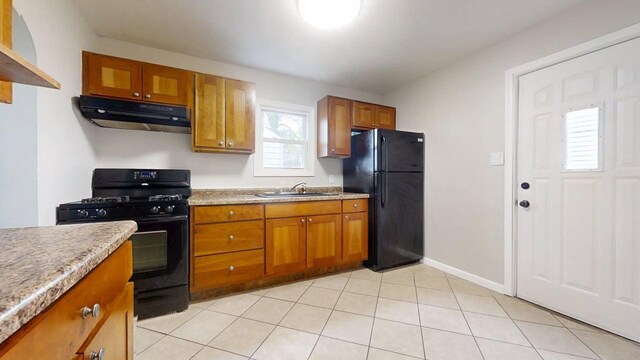 kitchen featuring brown cabinetry, light countertops, under cabinet range hood, a sink, and black appliances