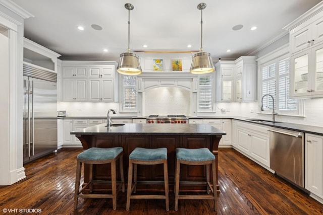 kitchen featuring stainless steel appliances, a kitchen island with sink, a sink, and dark countertops