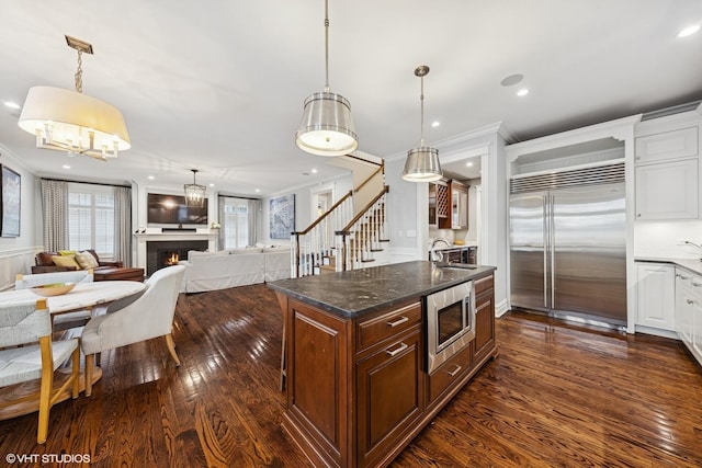 kitchen featuring built in appliances, dark wood-style flooring, crown molding, and a sink