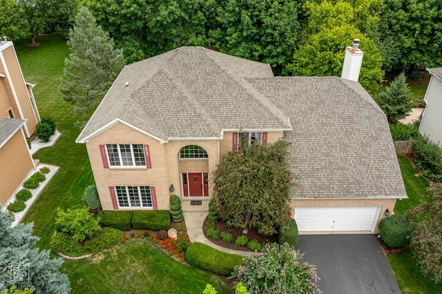 view of front of home featuring roof with shingles, an attached garage, a front yard, a chimney, and driveway