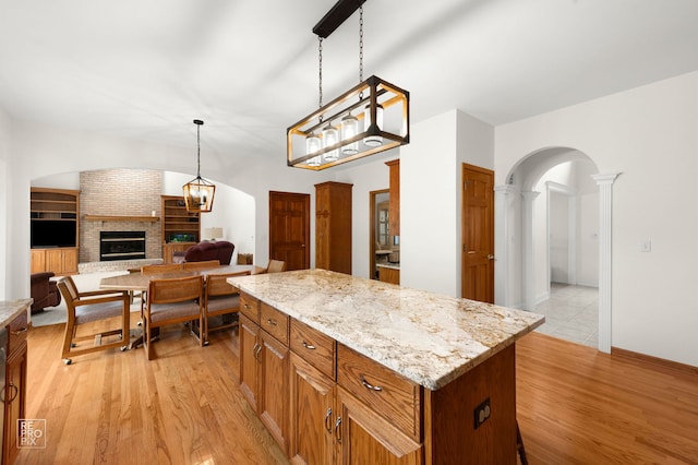kitchen featuring a brick fireplace, arched walkways, light wood finished floors, and a center island