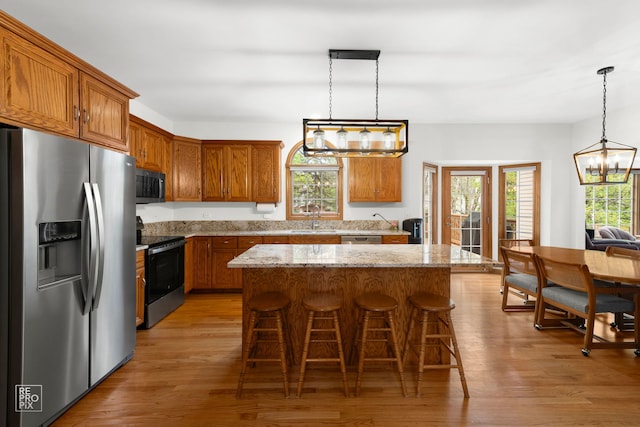 kitchen featuring appliances with stainless steel finishes, brown cabinetry, a sink, and light wood-style floors