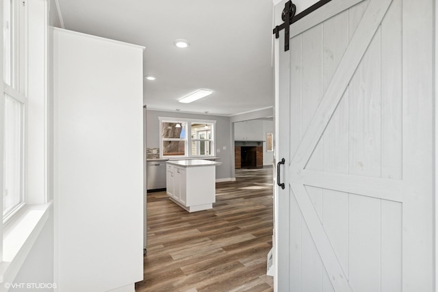hall featuring a barn door, wood finished floors, baseboards, and recessed lighting
