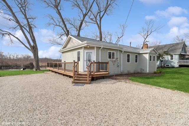 back of house with a chimney, a wooden deck, roof with shingles, and a lawn