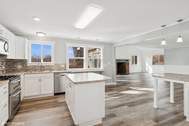 kitchen featuring stainless steel appliances, light wood-style flooring, a sink, light countertops, and a kitchen island