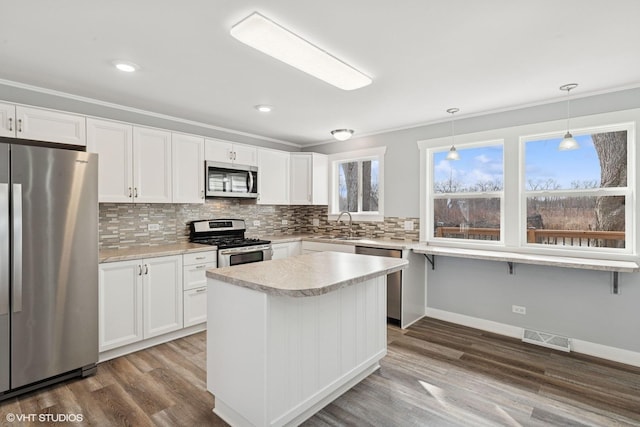 kitchen with wood finished floors, visible vents, a sink, decorative backsplash, and appliances with stainless steel finishes