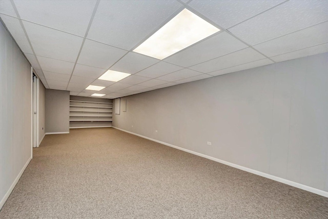 finished below grade area with a paneled ceiling, baseboards, and carpet floors