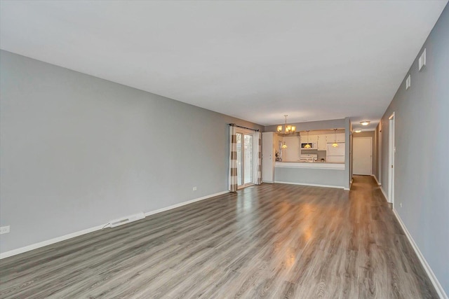 unfurnished living room with a chandelier, wood finished floors, and baseboards