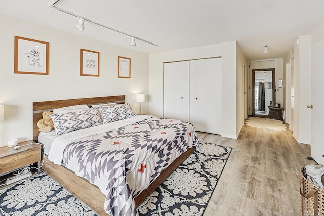 bedroom with a closet, light wood finished floors, baseboards, and track lighting